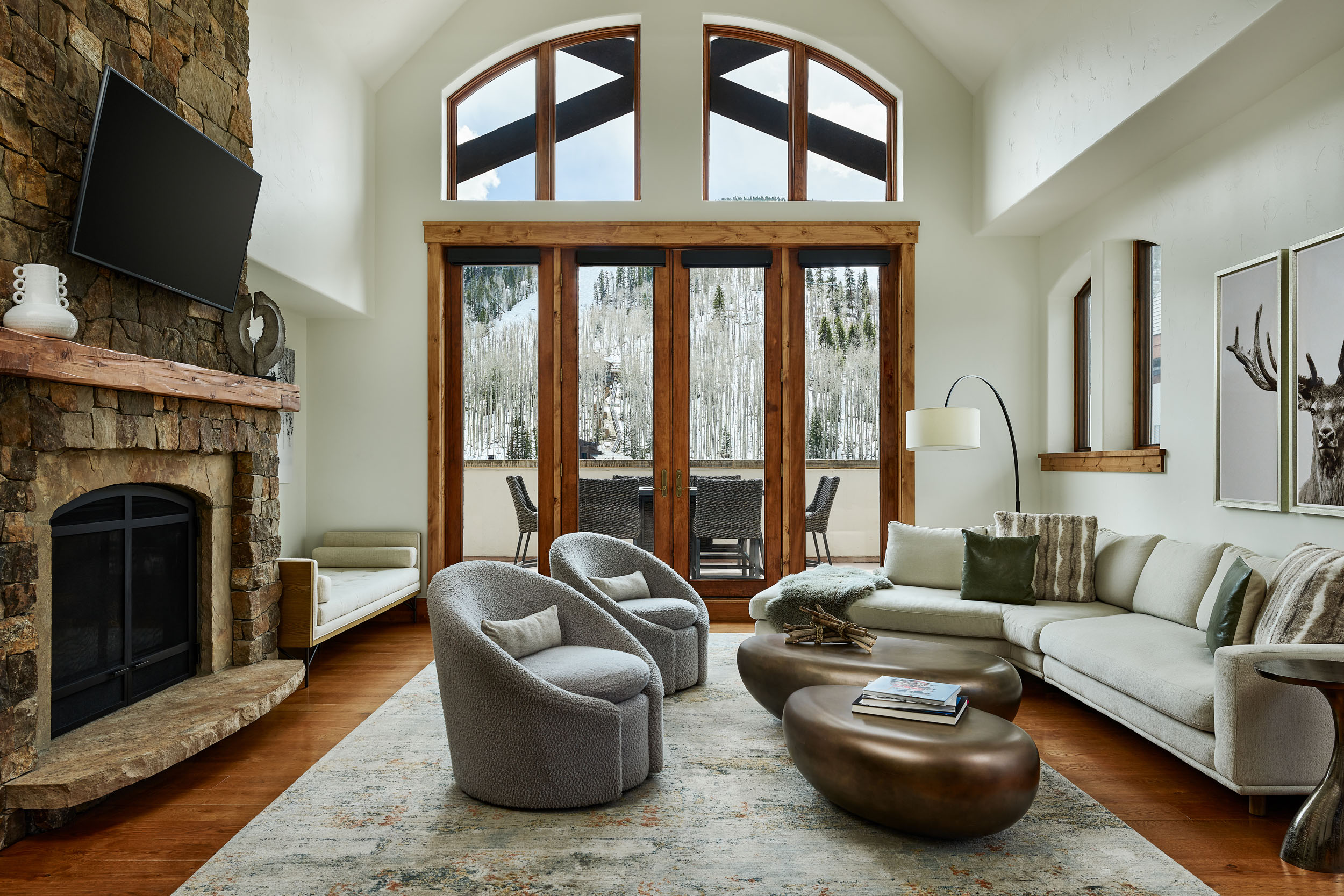 Luxury penthouse living room with a stone fireplace, vaulted ceilings, and large windows overlooking snowy Vail mountains.